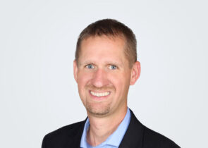 Headshot of Joshua Sales, a man with brown hair, in front of a light grey background.