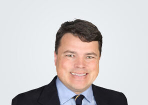 Headshot of Peter Symonds, a man with dark brown hair, in front of a light grey background.