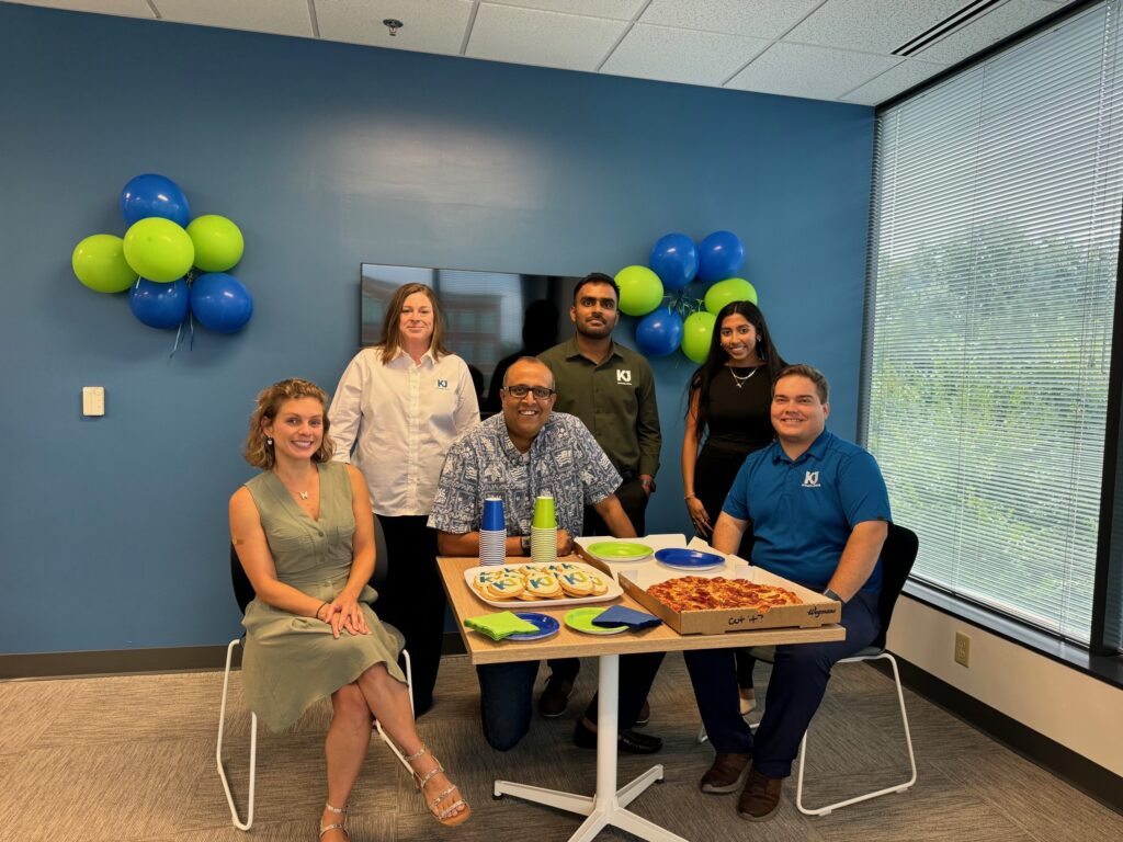 Christiana Tambone, Adrianna Dimperio, Aditya Ramamurthy, Sandesh Deshmukh, Muskan Amin and Eric Marshall celebrate KJ's new Mid-Atlantic office space. An open pizza box is on a central table.